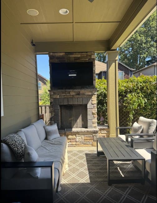 TV mounted above a stone outdoor fireplace on a covered patio, angled away from afternoon glare
