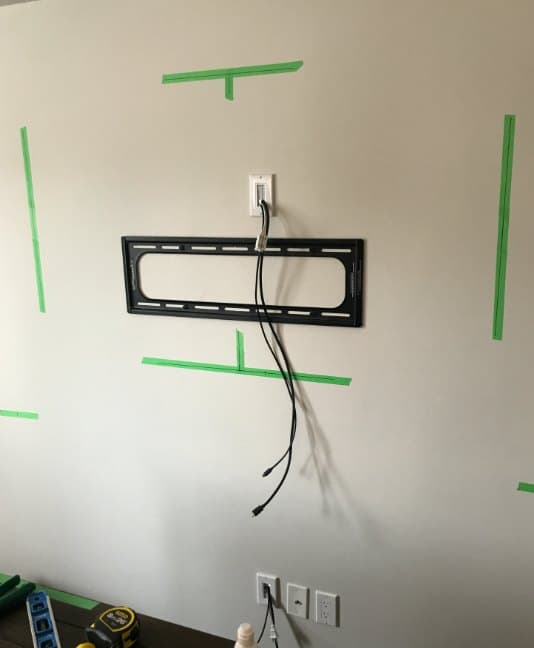 Wall bracket fitted with a recessed in-wall plate above it, power and HDMI dropping inside the wall to a second plate behind the media console, layout marked out in painter tape